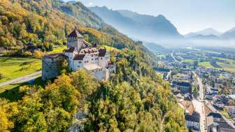 Schloss Vaduz, umgeben von herbstlich gefärbtem Wald, mit Blick auf das Rheintal