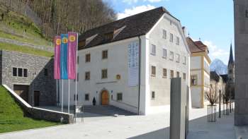 Außenansicht des Liechtensteinischen Landesmuseums in Vaduz mit bunten Fahnen und Blick auf die historische Fassade.