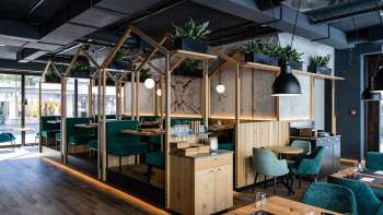 Modernes Restaurant mit stilvoller Holzkonstruktion, grünen Polstersitzen und kreativer Raumaufteilung
