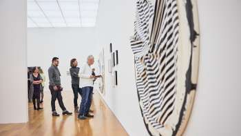 Besuchergruppe im Ausstellungsraum des Kunstmuseums, im Vordergrund ein großes, rundes Kunstwerk