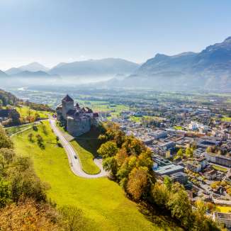 Luftaufnahme von Schloss Vaduz mit Blick über die Stadt Vaduz und das Rheintal an einem klaren Herbsttag
