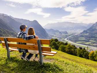Paar sitzt auf einer Bank in Triesenberg und blickt auf das Rheintal in Liechtenstein mit beeindruckendem Alpenpanorama