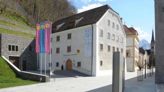 Außenansicht des Liechtensteinischen Landesmuseums in Vaduz mit bunten Fahnen und Blick auf die historische Fassade.